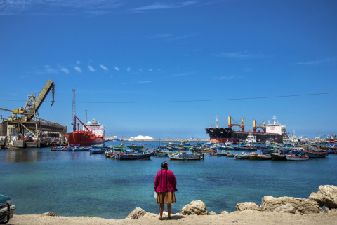  PERU – NOVEMBER 2014: Indian woman observing the arrival of a large cargo ship to Matarani’s port. The growth of this town has been steady with the construction of the Interoceanic Highway. In 2012, its port mobilized three million tonnes and is expected to increase as the company Tisur, which holds the concession for this port since 1999, plans to invest US $ 140 million to build a system for receiving, storage and shipment of minerals. These extensions will attend future mining projects in the central An